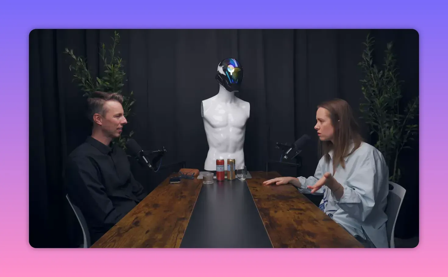 широкий кадр интервью: ведущий и гость за столом, гость жестикулирует, манекен между ними
