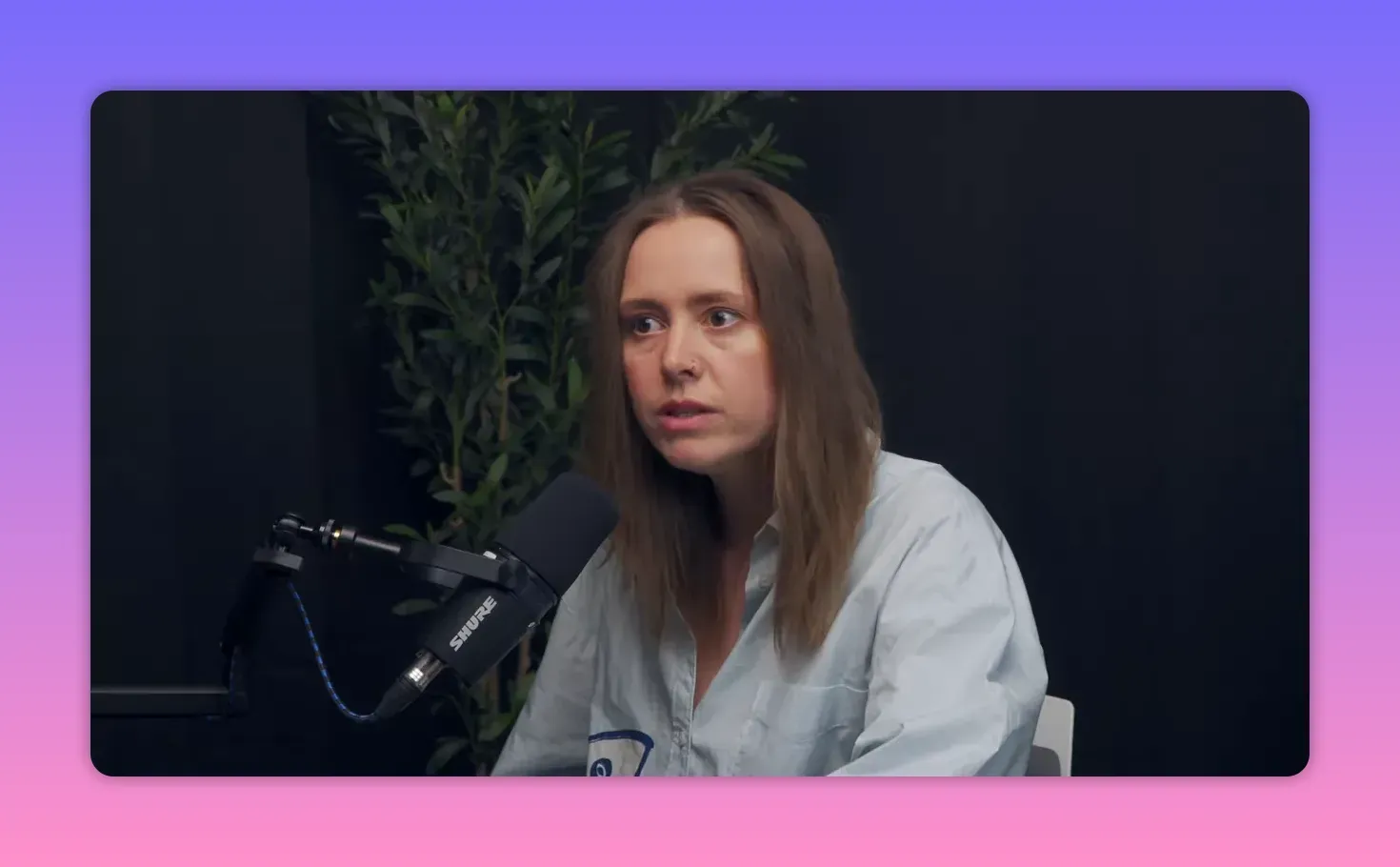 Крупный план участницы подкаста у микрофона, внимательный взгляд на тёмном фоне.