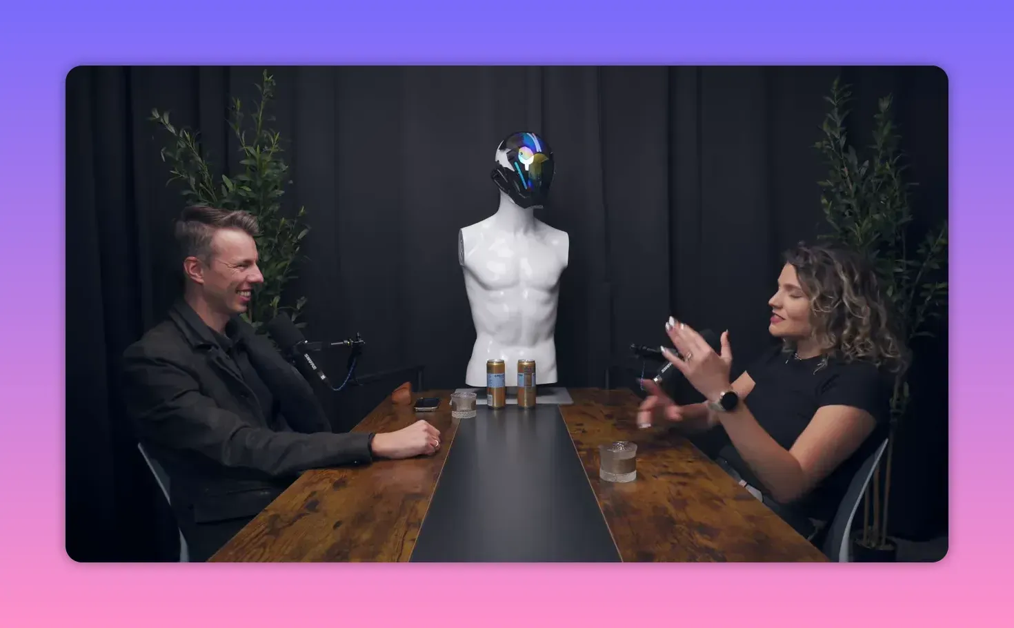 Широкий кадр интервью: женщина жестикулирует рукой, собеседник улыбается, студийная обстановка с микрофонами.